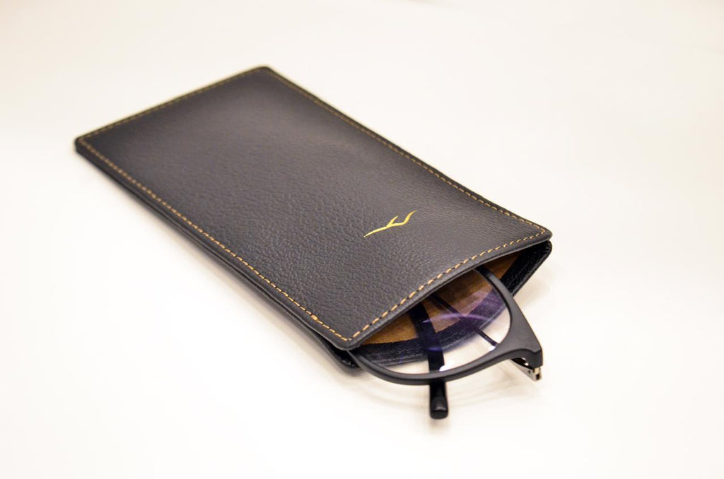 Close-up of the black camel leather eyeglasses pouch showing its slim profile and gold stitching