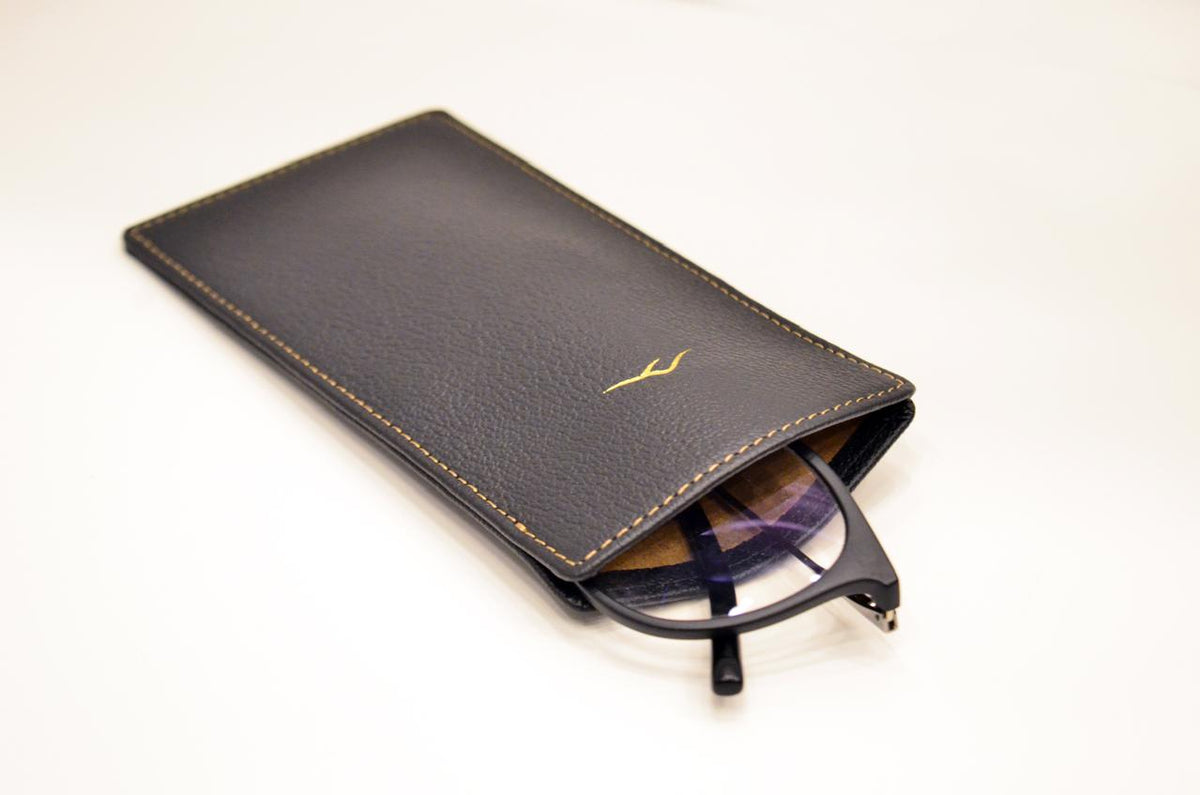 Close-up of the black camel leather eyeglasses pouch showing its slim profile and gold stitching